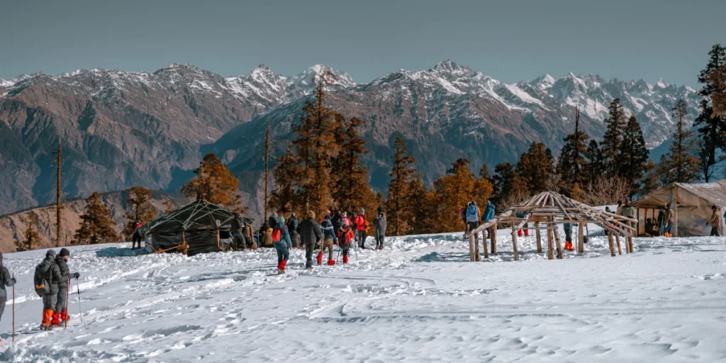 Tourists and skiers on snow-covered slopes at Auli with panoramic Himalayan peaks in the background — best time to visit Auli for skiing is December to March.